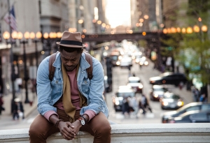 A young man alone sitting above a croweded street A young man alone sitting above a croweded street